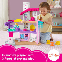 Toddler playing with Barbie dreamhouse playset featuring purple-and-pink house, slide, figures
