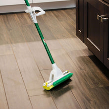 Sponge mop with scrub brush cleaning a wood-look floor, green handle and yellow pad.