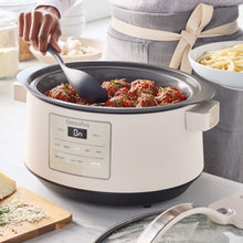 GreenPan slow cooker with lid open while serving spaghetti sauce with a ladle.