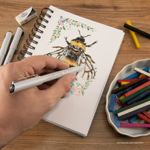 Mixed media paper pad open with bee sketch, hand drawing with white pen