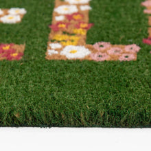 Outdoor coir doormat close-up, green texture with floral “HELLO” letters