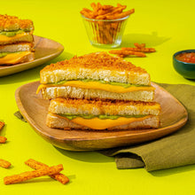 Stacked sandwiches on a wooden board with chips scattered and a dip cup
