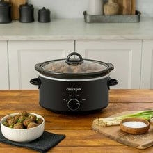 Black slow cooker on countertop with lid and front dial, with serving bowl nearby