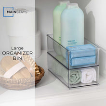 Stacked clear plastic organizer bins holding body wash bottles and folded towels
