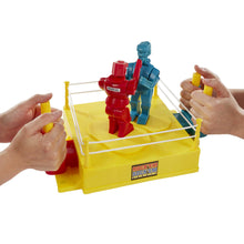 Hands holding pegs while red and blue robots stand on a yellow arena