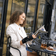 Black wrist brace worn by a person reading a magazine indoors