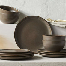 Brown stoneware dinner plate with speckled finish, shown stacked with other tableware