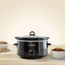 Black slow cooker with lid and front dial, with serving bowls placed beside it