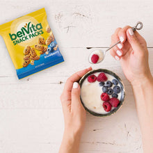 Hand holding a spoon above yogurt with berries beside a belVita snack pack
