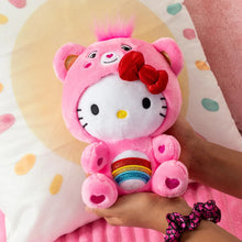 Pink cheer bear plush held in a hand, red bow and rainbow belly detail