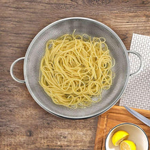 Perforated stainless steel colander with two side handles, holding pasta noodles