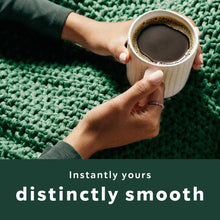 Hands holding a mug of instant coffee on a green textured blanket