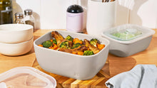 Taupe stoneware bake and store bowl with clear lid, filled with roasted vegetables