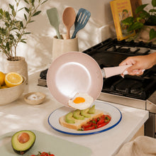 Rose ceramic non-stick frying pan cooking egg on stovetop with spatula and utensils