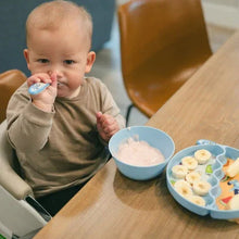 Baby using a suction bowl and spoon from a mealtime set on table
