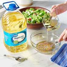 Vegetable oil bottle with blue cap pouring golden oil into a glass mixing bowl.