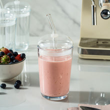 Clear glass dome-lid tumbler filled with pink drink, with straw