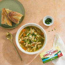 Salted butter half sticks pack beside soup bowl, bread pieces, and herbs