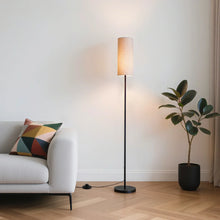 Black LED floor lamp with beige fabric shade, standing next to sofa and plant