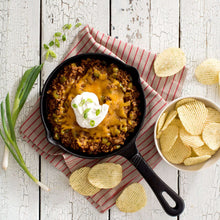 Skillet of cheesy dip with sour cream, tortilla chips, and diced vegetables