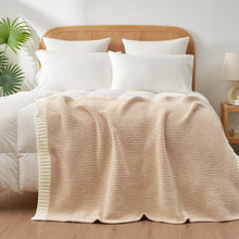 Beige knitted throw blanket on bed, neatly draped across bedding with quilted texture.