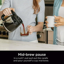 Coffee maker carafe being pulled out while pouring brewed coffee into mugs