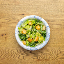 Disposable paper bowl filled with salad greens and croutons