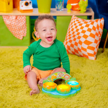 Baby on a rug with a green musical drum toy and three colorful drum pads on a jungle ring