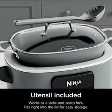 Gray multi-cooker with glass lid and included utensil resting on top