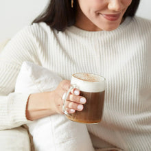 Glass mug of dark coffee with foam, held in hands