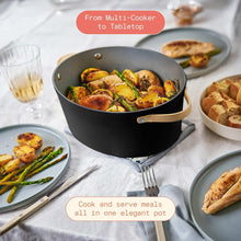 Black multi-cooker pot with lid and gold-tone handles, filled with vegetables