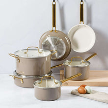 Nonstick cookware set with taupe pans, stainless pieces, gold handles, and a skillet