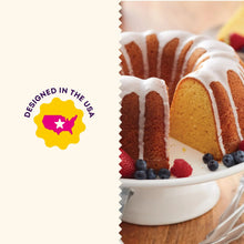 Bundt cake with white icing drips and berries on a white stand