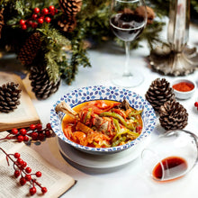 Printed paper bowl with blue floral rim holding pasta and sauce