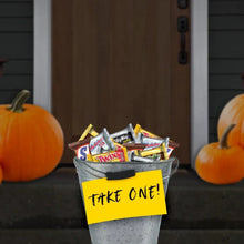 Mini chocolate candy bars in a metal bucket with pumpkins on a doorstep