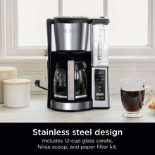 Stainless steel and black coffee maker with glass carafe, display panel, and mugs