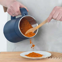 Blue electric grinder with lid open, pouring ground spice into a plate