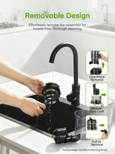 Black juicer with removable parts while being rinsed under running water at sink.