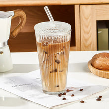 Ribbed glass tumbler with glass lid and straw filled with iced coffee and beans.