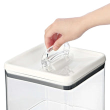 Airtight bagel food storage container with flip latch being lifted by hand, clear body