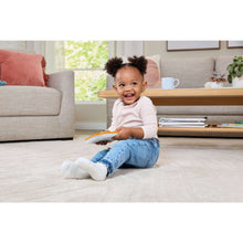 Infant sitting on floor smiling while holding an orange learning tablet toy