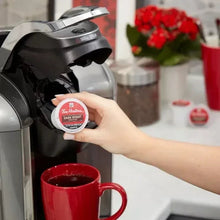 Hand placing Tim Hortons K-Cup pod into Keurig with red mug