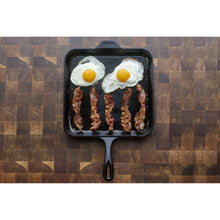 Square cast iron griddle with two fried eggs and bacon strips