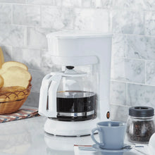White coffee maker on counter with glass carafe and black warming plate