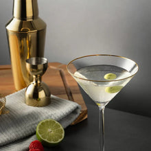 Gold-rim martini glass filled with clear drink and lime slices on clear stem