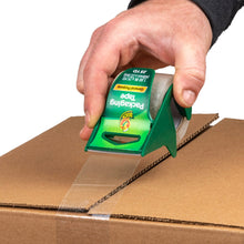 Manual packaging tape dispenser applying clear tape strip to cardboard box seam