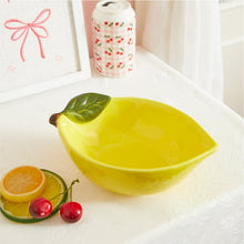 Yellow ceramic lemon bowl with green leaf handle and nearby citrus slices