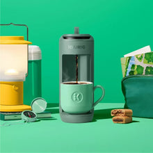 Compact single-serve pod coffee maker with mug, green body, pouring coffee