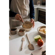 Taupe ceramic bakeware ramekin cup with whisk and spatulas on a countertop