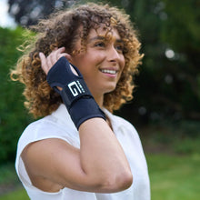 Black wrist brace worn on the wrist with hand near the face outdoors